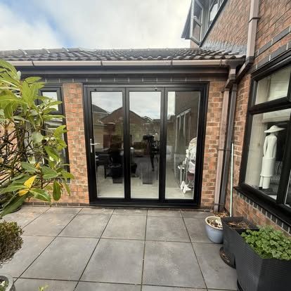 Black three-pane glazed doors opening from a brick rear extension onto a paved patio