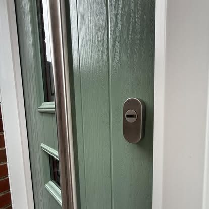 Close-up of a green woodgrain composite door showing the stainless bar handle and cylinder lock